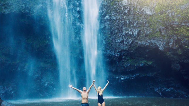 Couple enjoying pool at the base of large waterfall in Hawaii